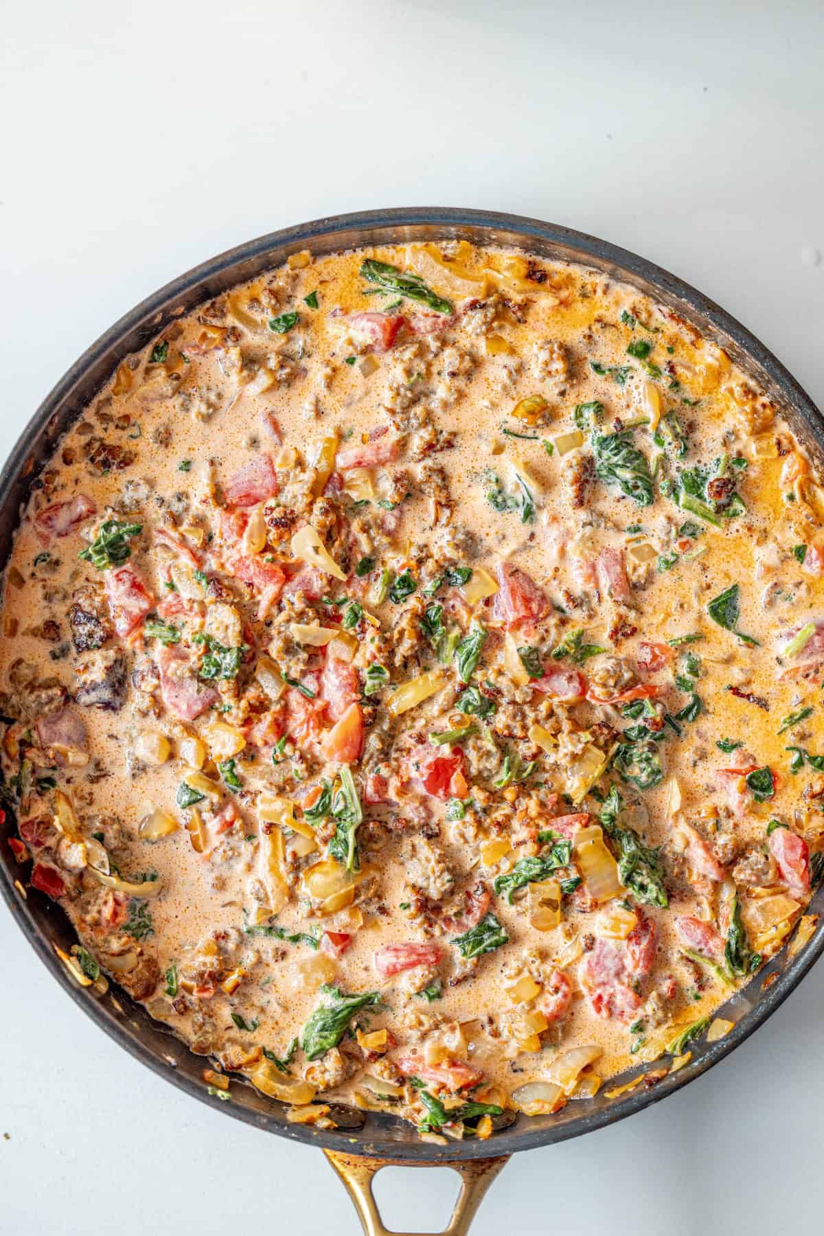 A skillet filled with a creamy mixture of ground meat, chopped tomatoes, spinach, onions, and herbs—perfect inspiration for a ravioli with tomato spinach cream sauce.