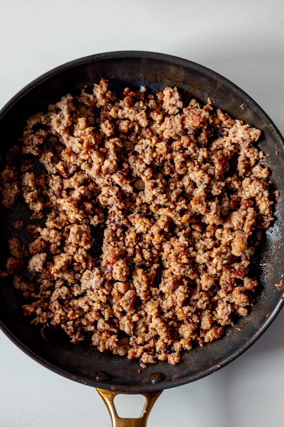 Cooked ground beef in a black skillet on a light-colored surface, ready to be added to your favorite tomato cream sauce ravioli for a hearty meal.