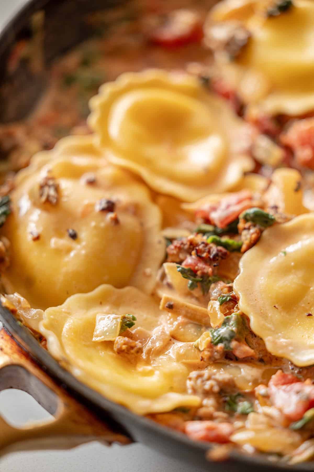 A close-up of tomato cream sauce ravioli in a skillet, featuring spinach, sun-dried tomatoes, and onions in a rich, creamy blend.