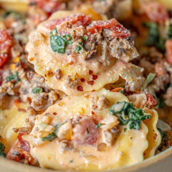 Close-up of ravioli pasta with ground meat, spinach, diced tomatoes, and a creamy sauce, topped with red pepper flakes—a delicious ravioli with tomato spinach cream sauce.