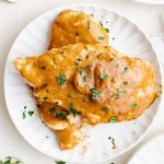A plate with chicken covered in creamy garlic sauce.
