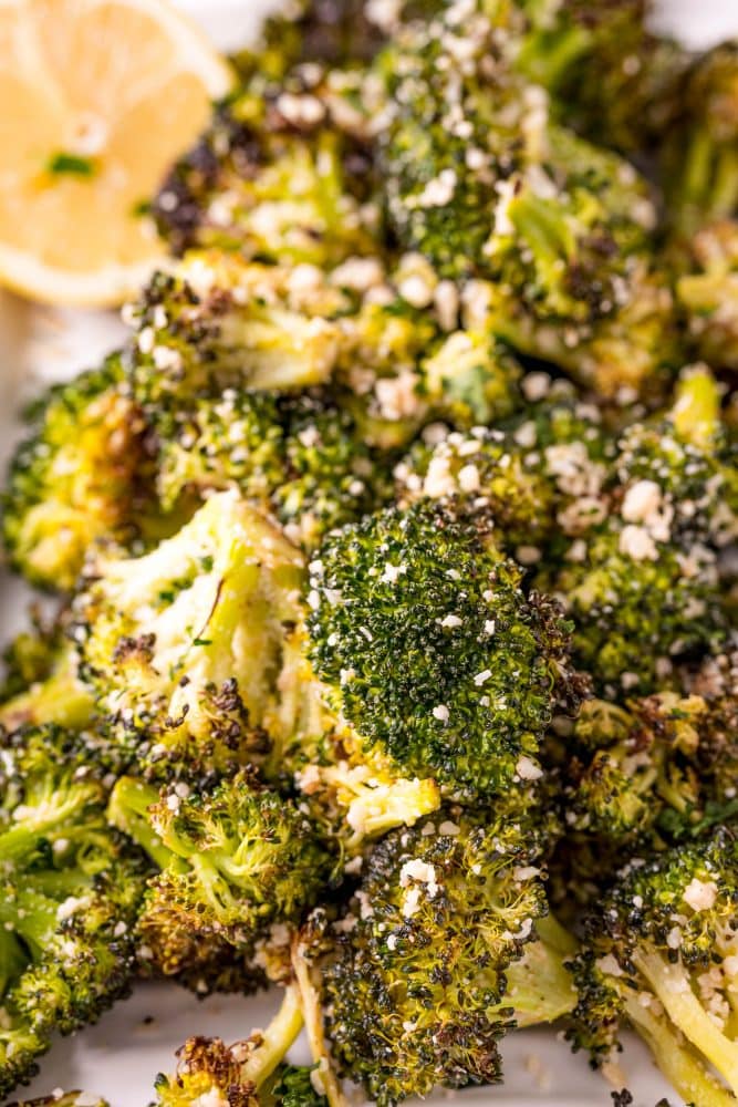 cooked broccoli on a white plate with parmesan on it and lemon in the corner