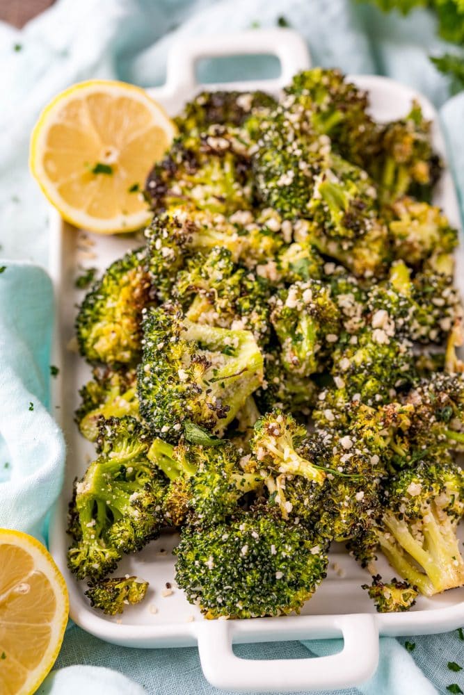 cooked broccoli on a white plate with parmesan on it and lemon in the corner