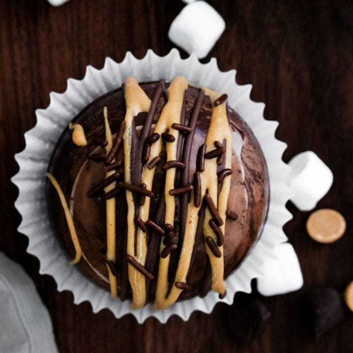 A peanut butter hot chocolate bomb-inspired chocolate cupcake with marshmallows and chocolate drizzle.