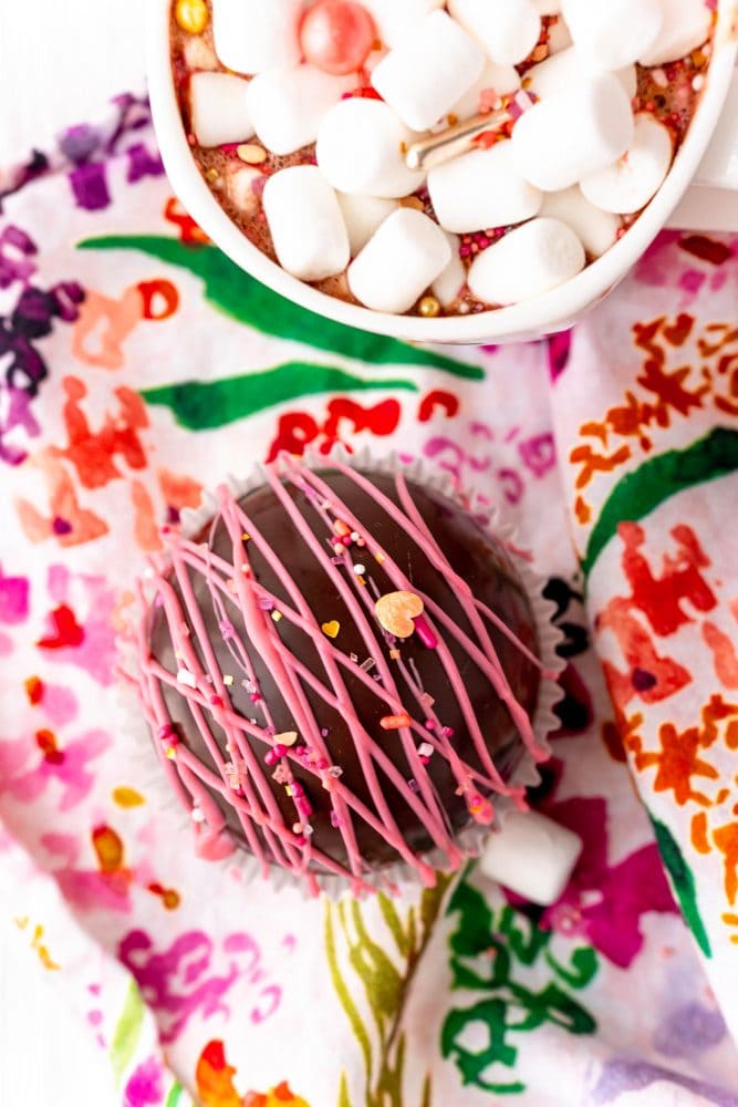 chocolate ball with pink frosting and sprinkles on it, hot chocolate next to it