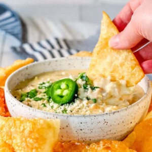 A person dipping a tortilla chip into a bowl of homemade white queso dip.