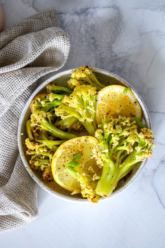 baby cauliflower and lemon slices in a white bowl on a marble countertop. 