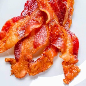 A close up of bacon baked in the oven on a white plate.