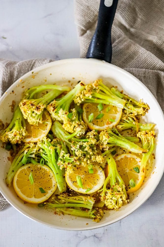 baby cauliflower and lemon slices in a white skillet on a marble countertop