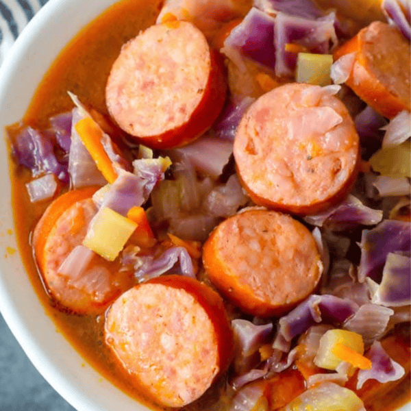 A bowl of savory sausage and red cabbage, accompanied by chopped vegetables, immersed in a rich broth—an easy cabbage and sausage soup perfect for those seeking a delicious keto-friendly option.