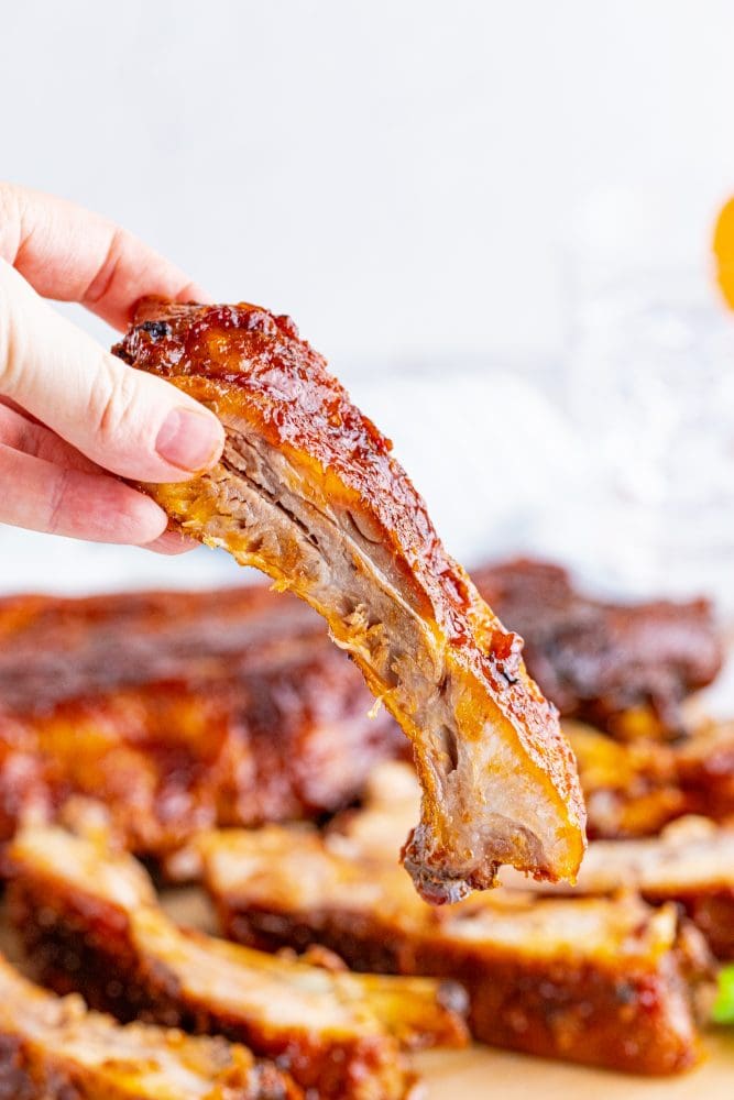 picture of a hand holding a grilled rib with bbq sauce slathered on it