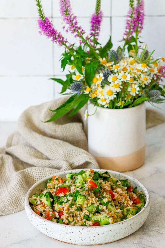 picture of tabbouleh in a dish on a table in front of wildflowers