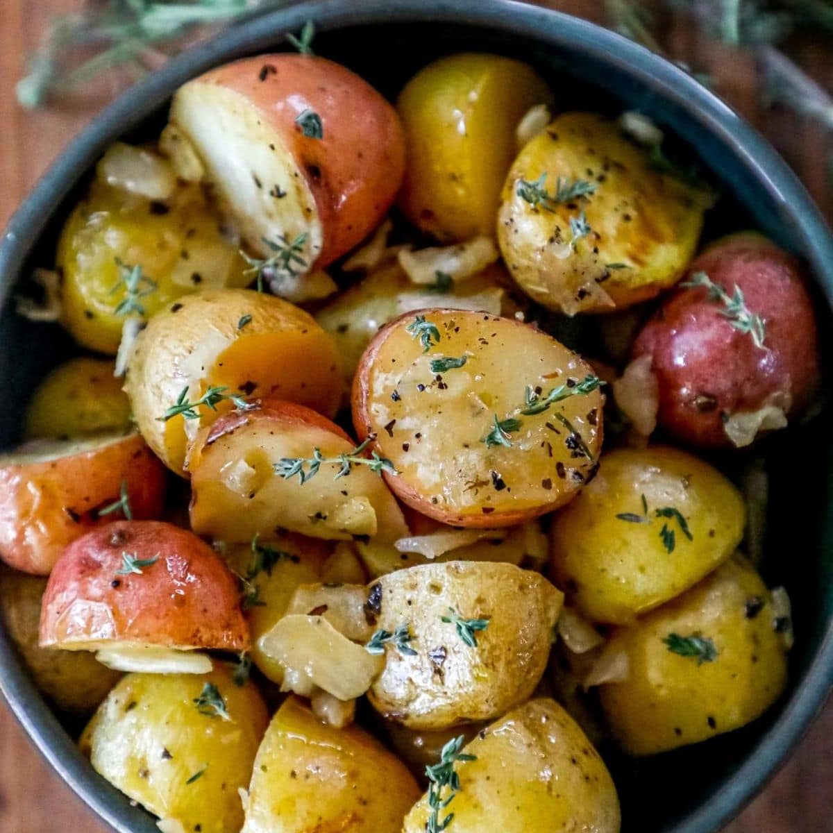 picture of roasted potatoes with butter, spices, and sprigs of fresh thyme in a bowl