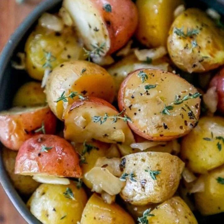 picture of garlic butter roasted potatoes in a blue bowl with herbs on top