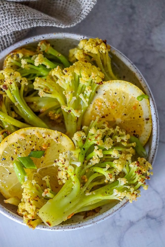 baby cauliflower and lemon slices in a white bowl on a marble countertop. 