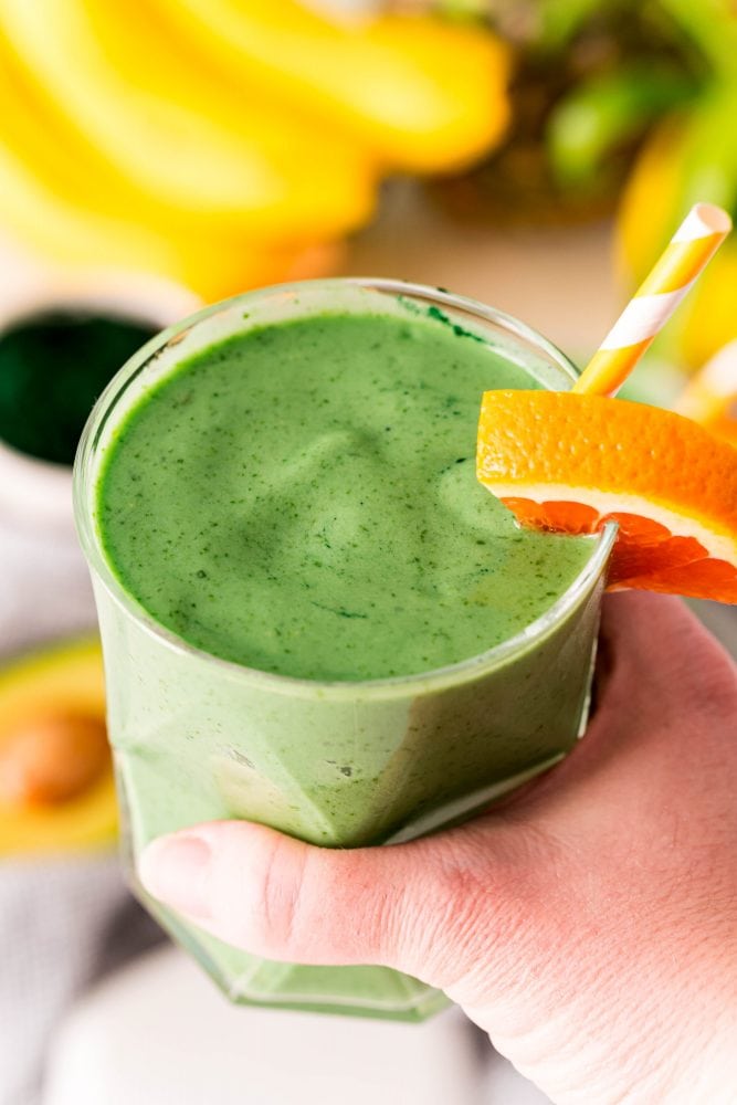 picture of green tropical smoothie with an orange slice and yellow straw