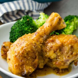 Chicken thighs and broccoli on a white plate, coated with mustard.