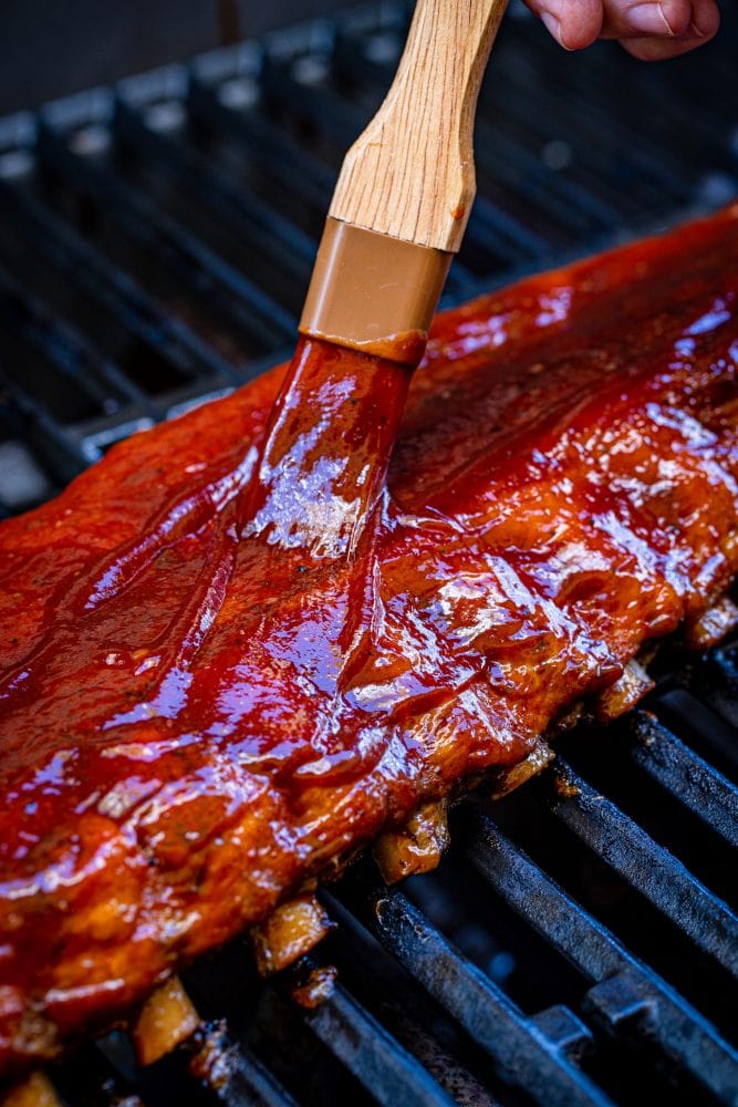 basting brush adding sauce to ribs on a grill
