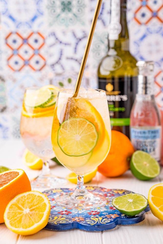 picture of a wine goblet with slices of citrus, ice, port, and tonic on a table