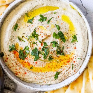 A bowl of hummus with pita chips and parsley, served alongside an easy baba ganoush recipe.