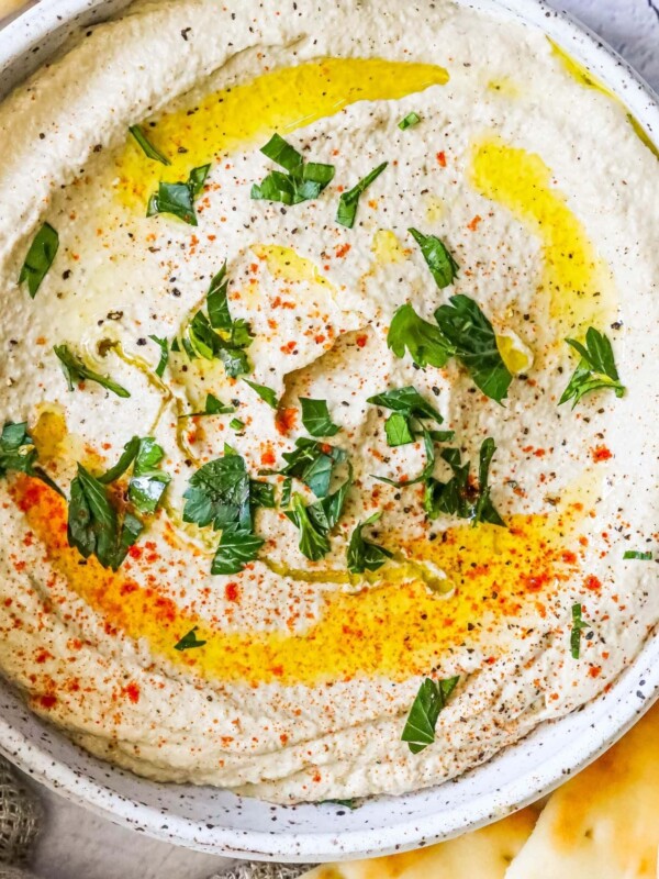 A bowl of hummus with pita chips and parsley, served alongside an easy baba ganoush recipe.