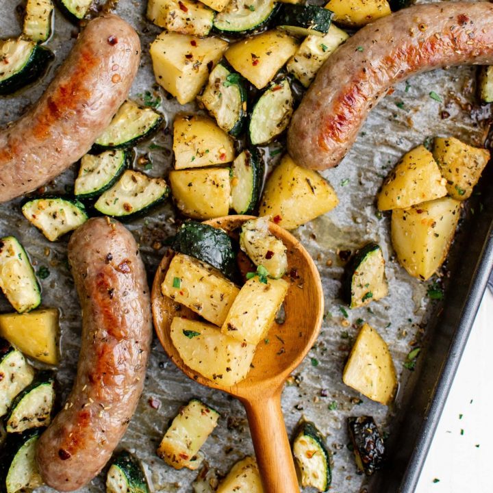 Sheetpan sausage bake recipe with potatoes and wooden spoon.