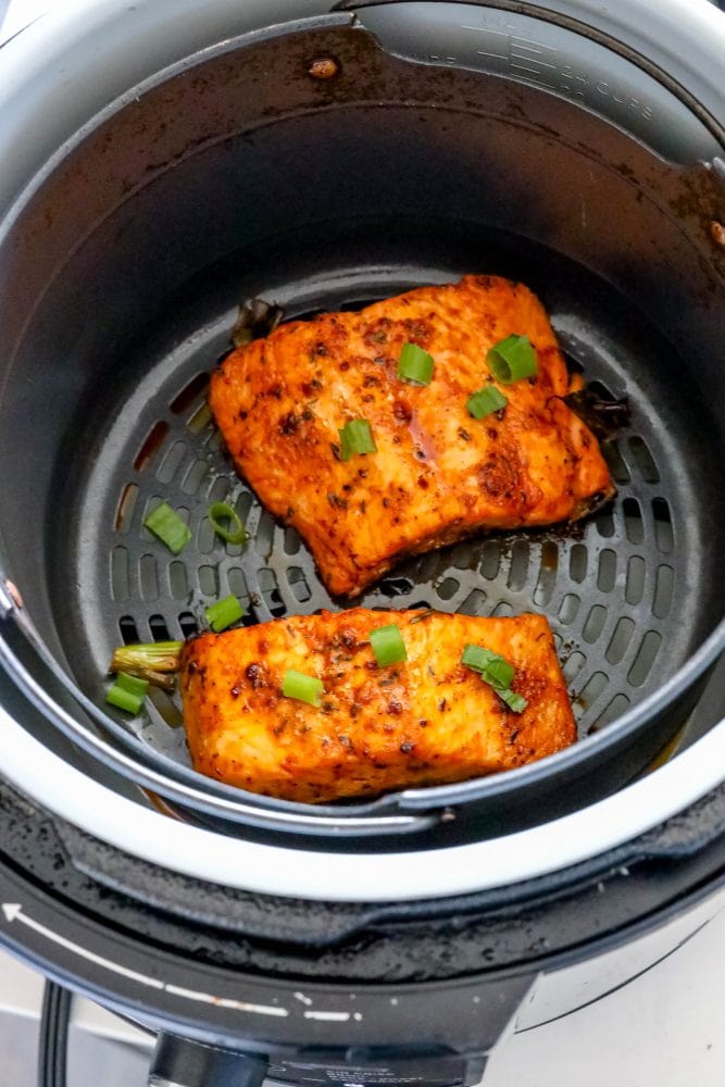 salmon with spices cooked in an air fryer basket with green onions on it