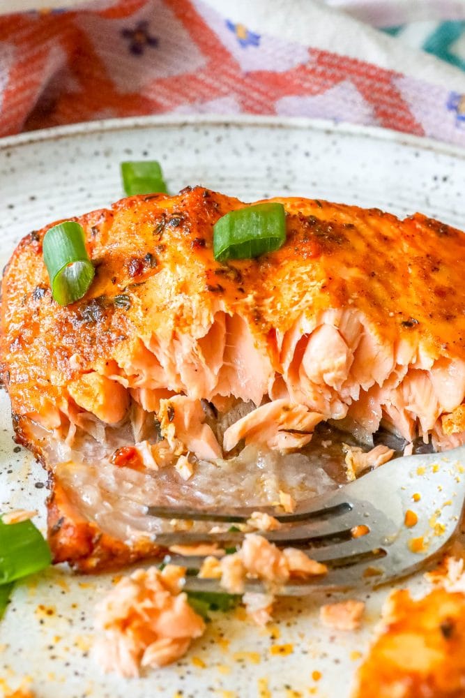salmon with spices cooked on a white plate with green onions on it with some eaten