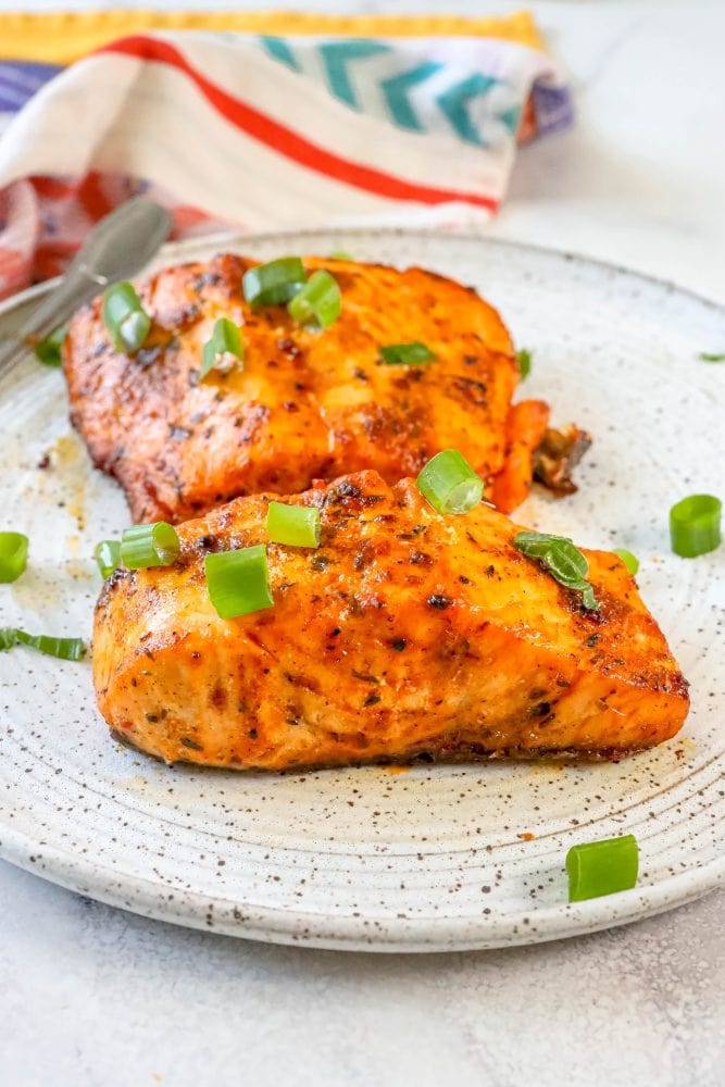 salmon with spices cooked on a white plate with green onions on it