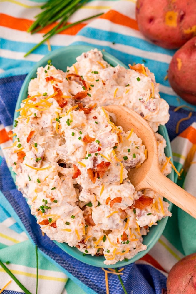 creamy ranch potato salad in a blue bowl on a colorful towel with a spoon in it