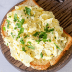 A slice of bread topped with creamy egg salad, from The Best Classic Egg Salad Recipe, garnished with chopped parsley and a sprinkle of ground black pepper.