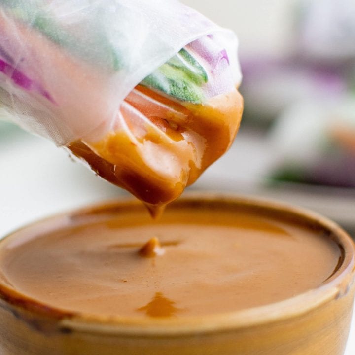 A bowl of peanut sauce being poured into a bowl, using an easy peanut sauce recipe.
