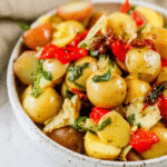 A bowl of vegan Italian potato salad with baby potatoes, red bell peppers, artichoke hearts, herbs, and sun-dried tomatoes—an Italian potato salad recipe with oil, not mayo.