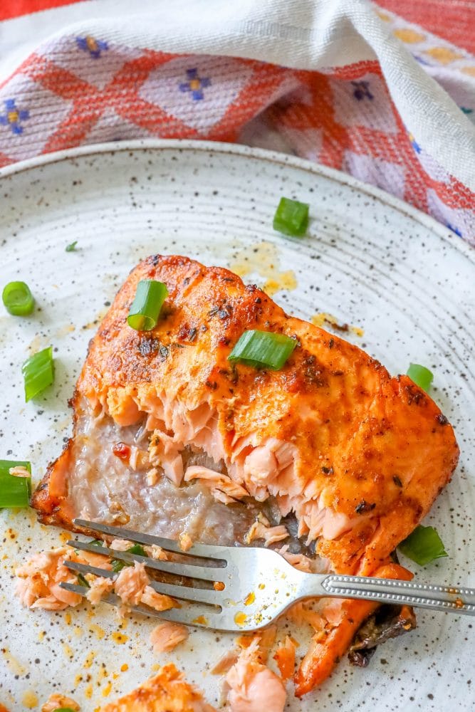 salmon with spices cooked on a white plate with green onions on it partially eaten