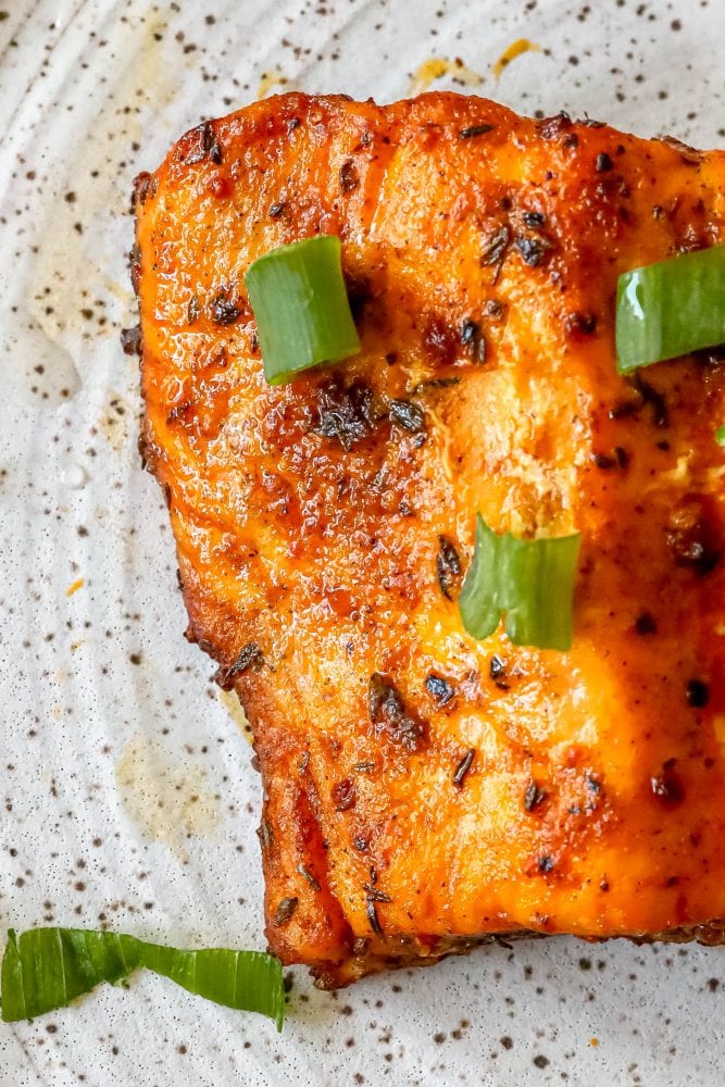 salmon with spices cooked on a white plate with green onions on it