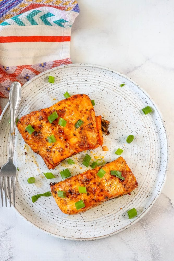 salmon with spices cooked on a white plate with green onions on it