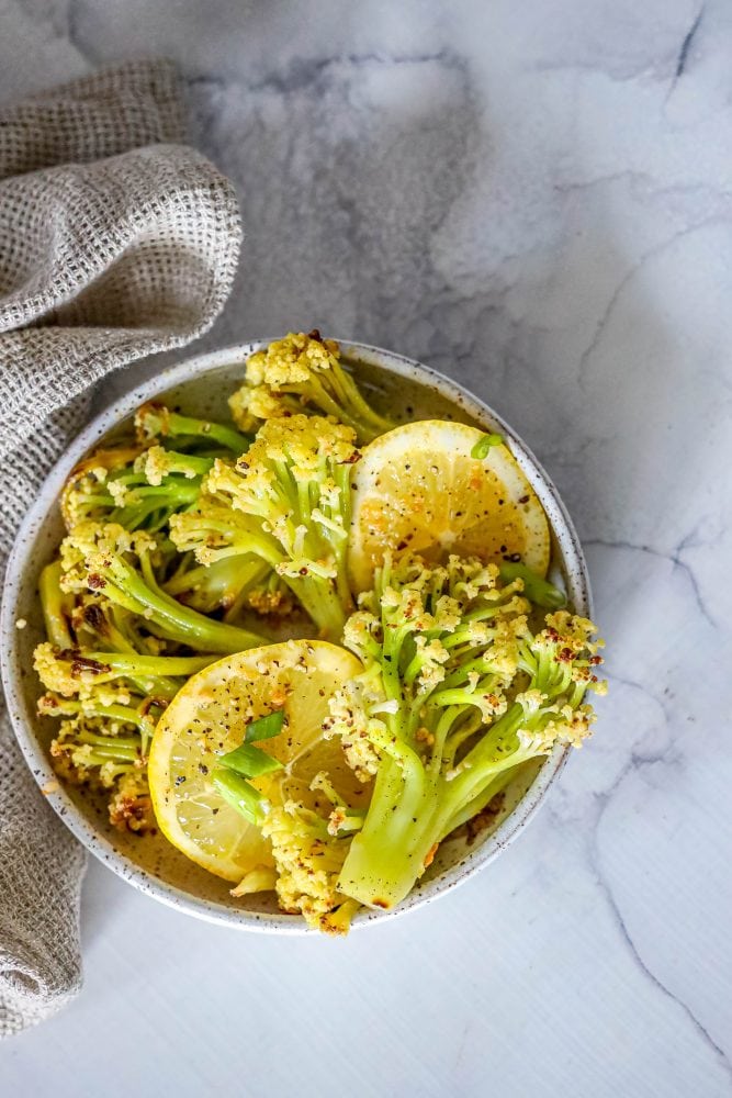 baby cauliflower and lemon slices in a white bowl on a marble countertop. 