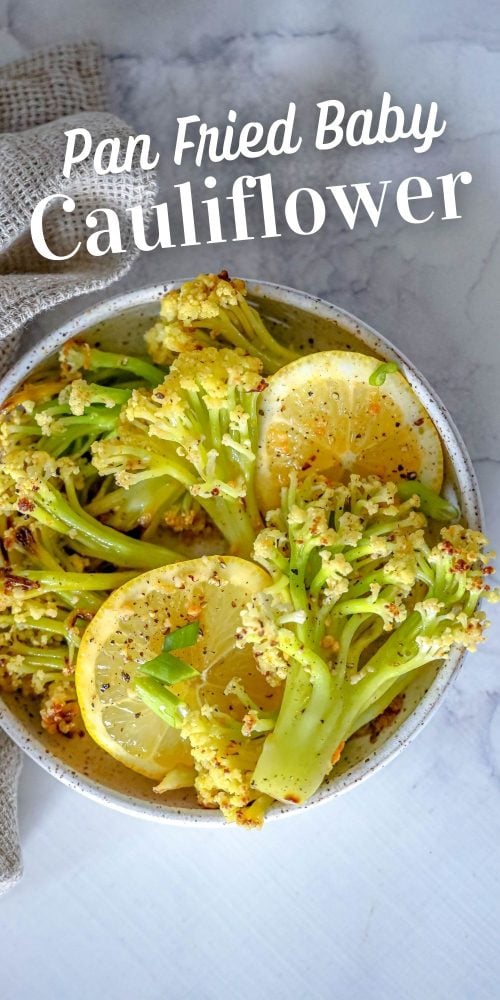 baby cauliflower and lemon slices in a white bowl on a marble countertop. 