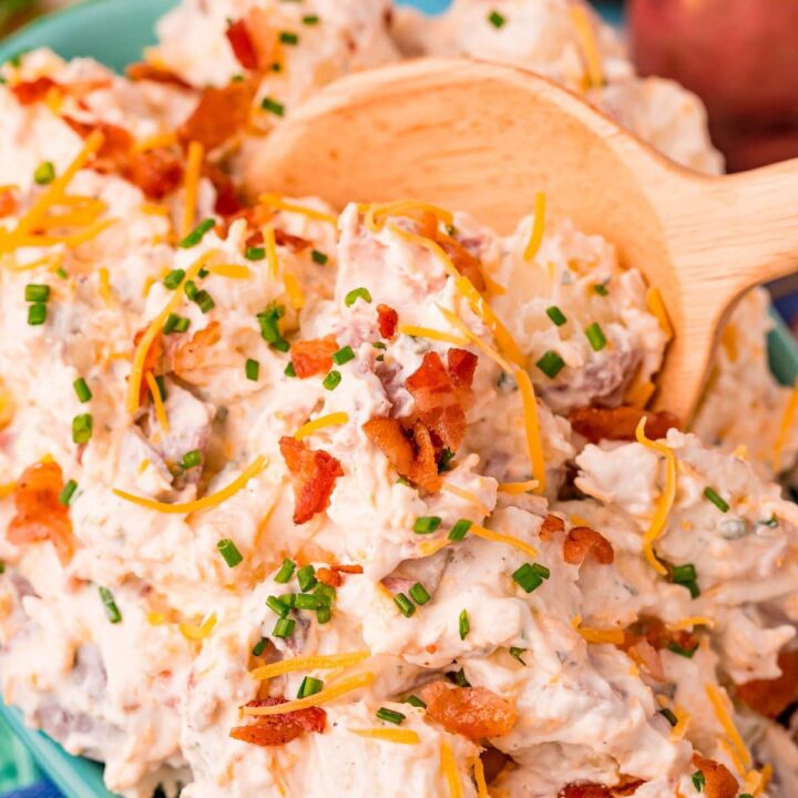 creamy ranch potato salad with chopped chives and crumbled bacon being scooped with a wooden spoon