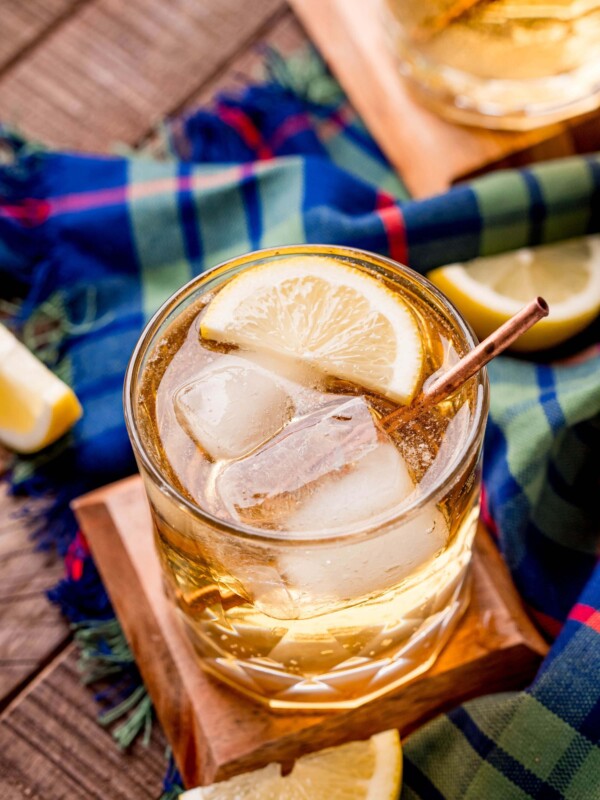A Scotch cocktail with ice and lemon garnish on a wooden table.