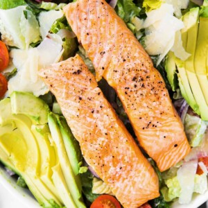 A ceasar salad with salmon, avocado and tomatoes.
