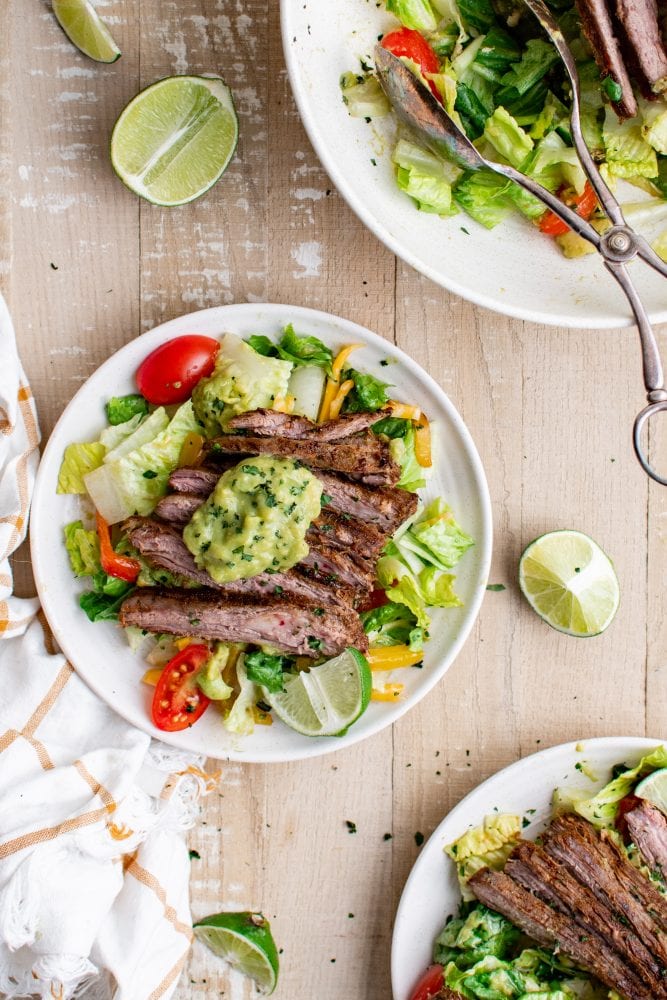 picture of steak fajita salad with guacamole on a white plate on a table