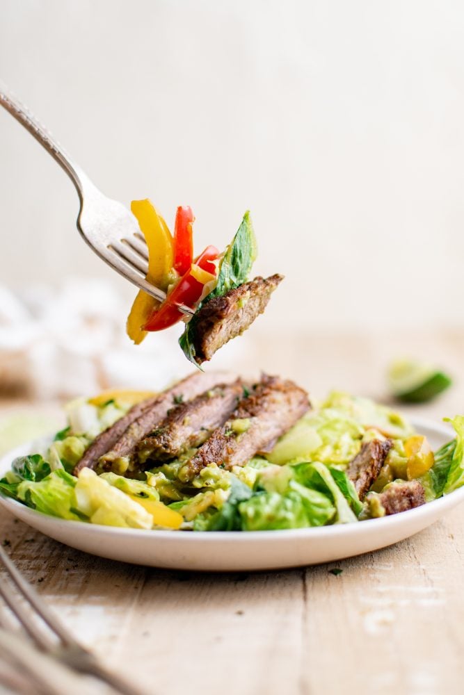 picture of steak fajita salad with guacamole on a white plate on a table