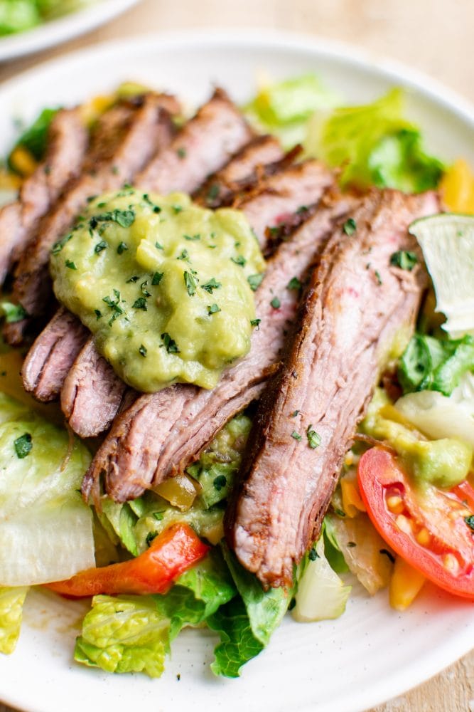 picture of steak fajita salad with guacamole on a white plate on a table