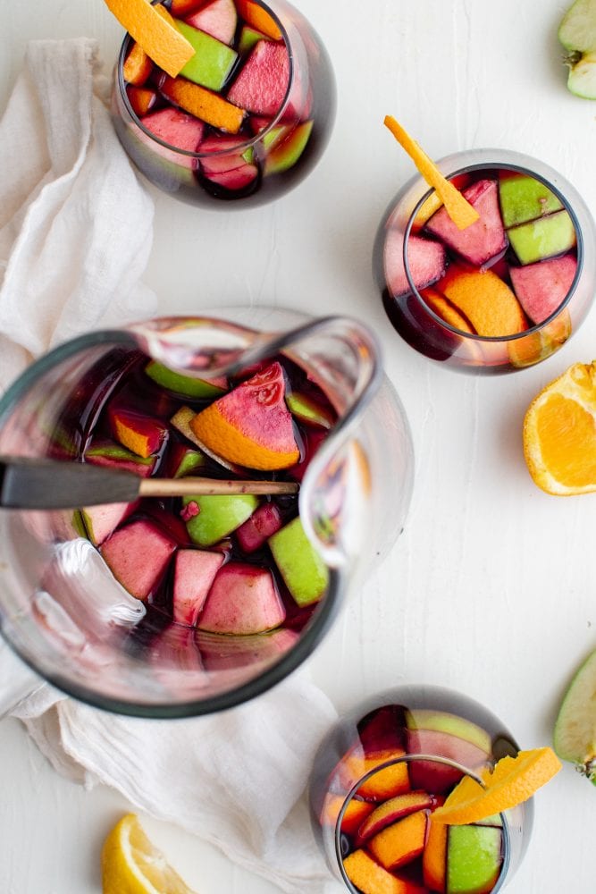 Glass of wine with fruit in it and a slice of orange on the side