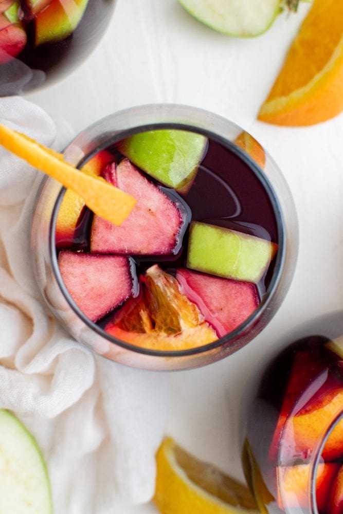 Glass of wine with fruit in it and a slice of orange on the side