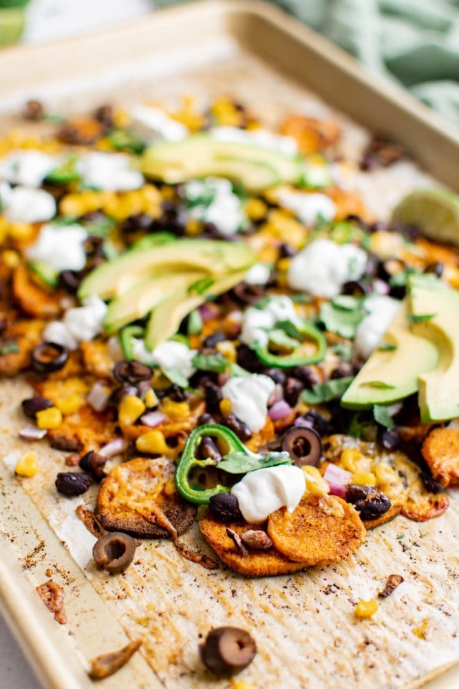 picture of sweet potato chip nachos on a plate with jalapenos, beans, corn, cheese, sour cream, avocados, and sliced limes