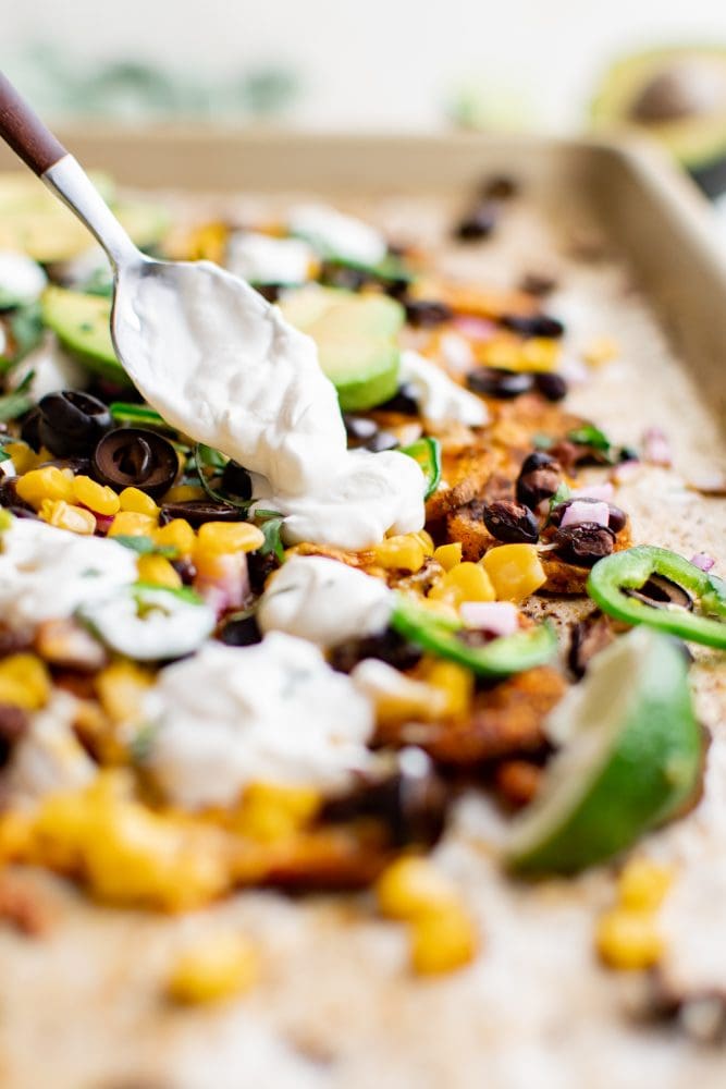 picture of sweet potato chip nachos on a plate with jalapenos, beans, corn, cheese, sour cream, avocados, and sliced limes