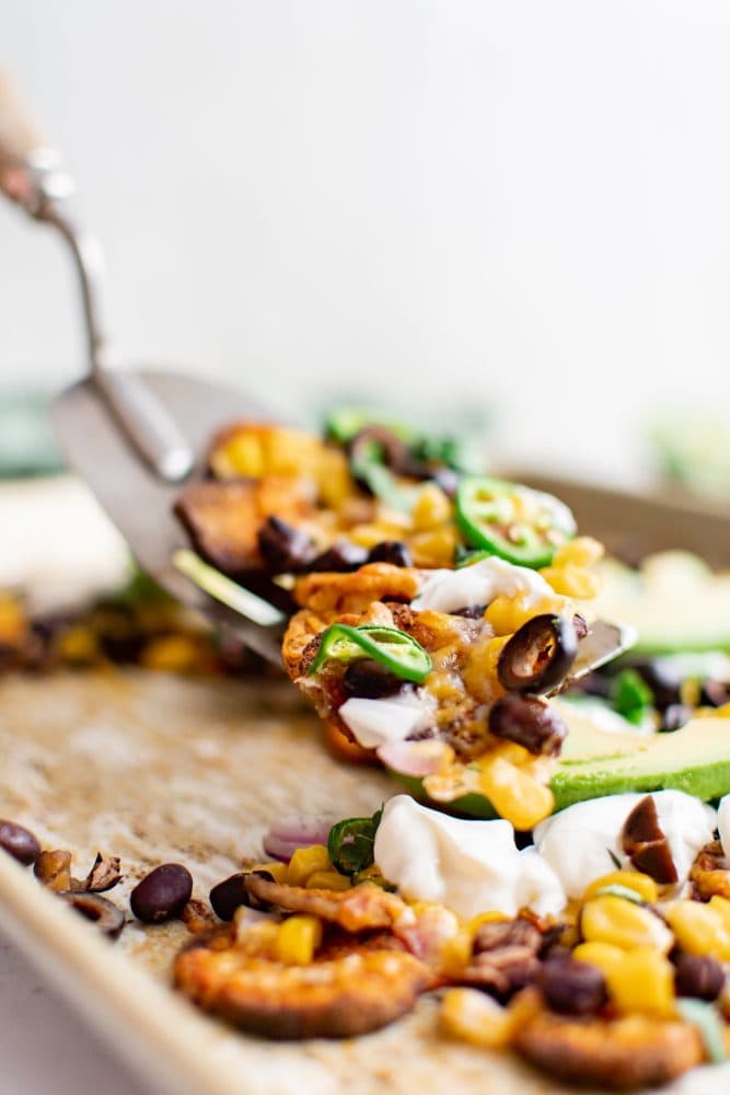 picture of sweet potato chip nachos on a plate with jalapenos, beans, corn, cheese, sour cream, avocados, and sliced limes