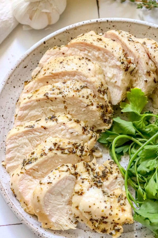 sliced chicken breast with herbs on a plate next to greens